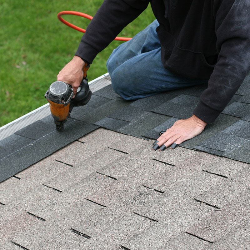 A person works on replacing roof shingles on a home