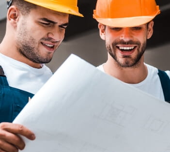 two men in hard hats, presumably home remodelers, look at a large sheet of paper