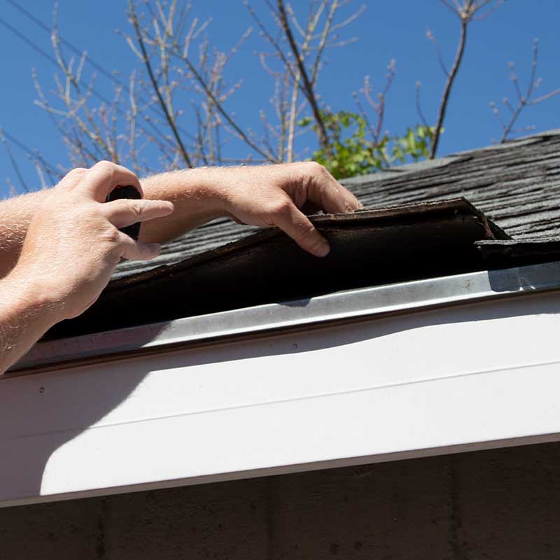 a person works on repairing the shingles on the roof of a house