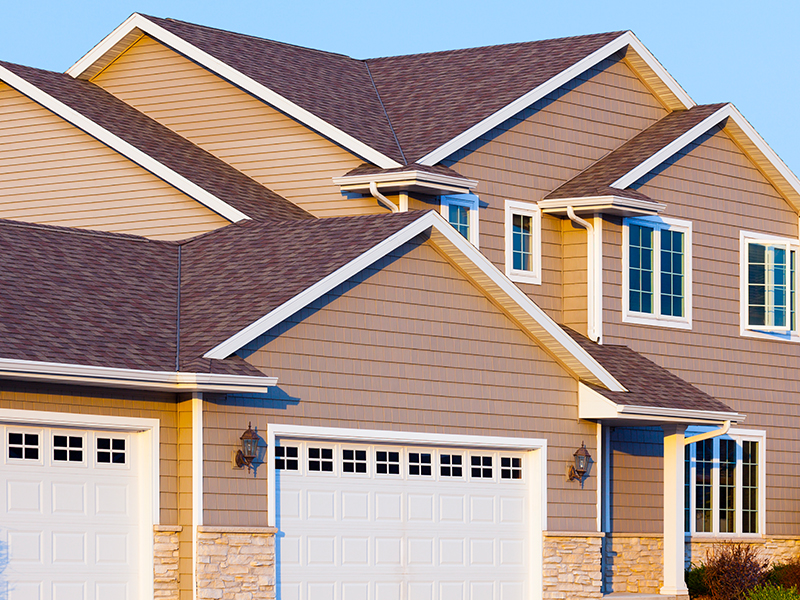 two roofing contractors with yellow hard hats and hammering shingles into a home's roof