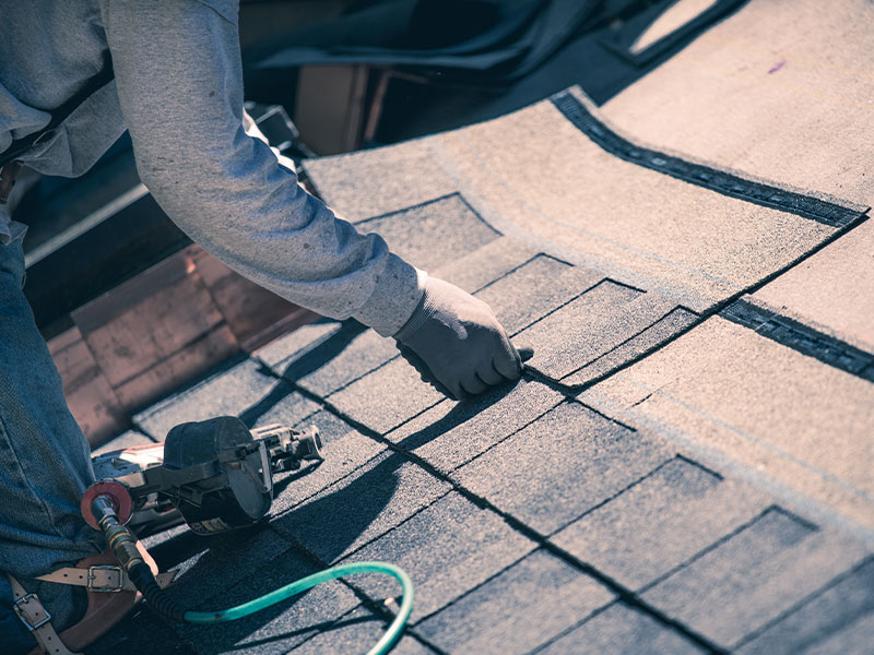 a roofing contractor lays shingles down on the roof of a house