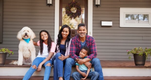 stock photo of a family of four with a large white dog sitting on the stairs of their front porch